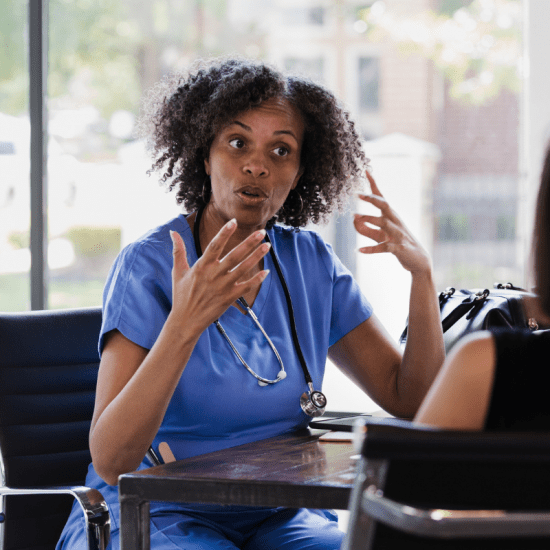 Nurse in blue scrubs talking to woman at table