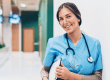 Nurse with brown hair smiling and wearing scrubs with a stethoscope and holding a clipboard
