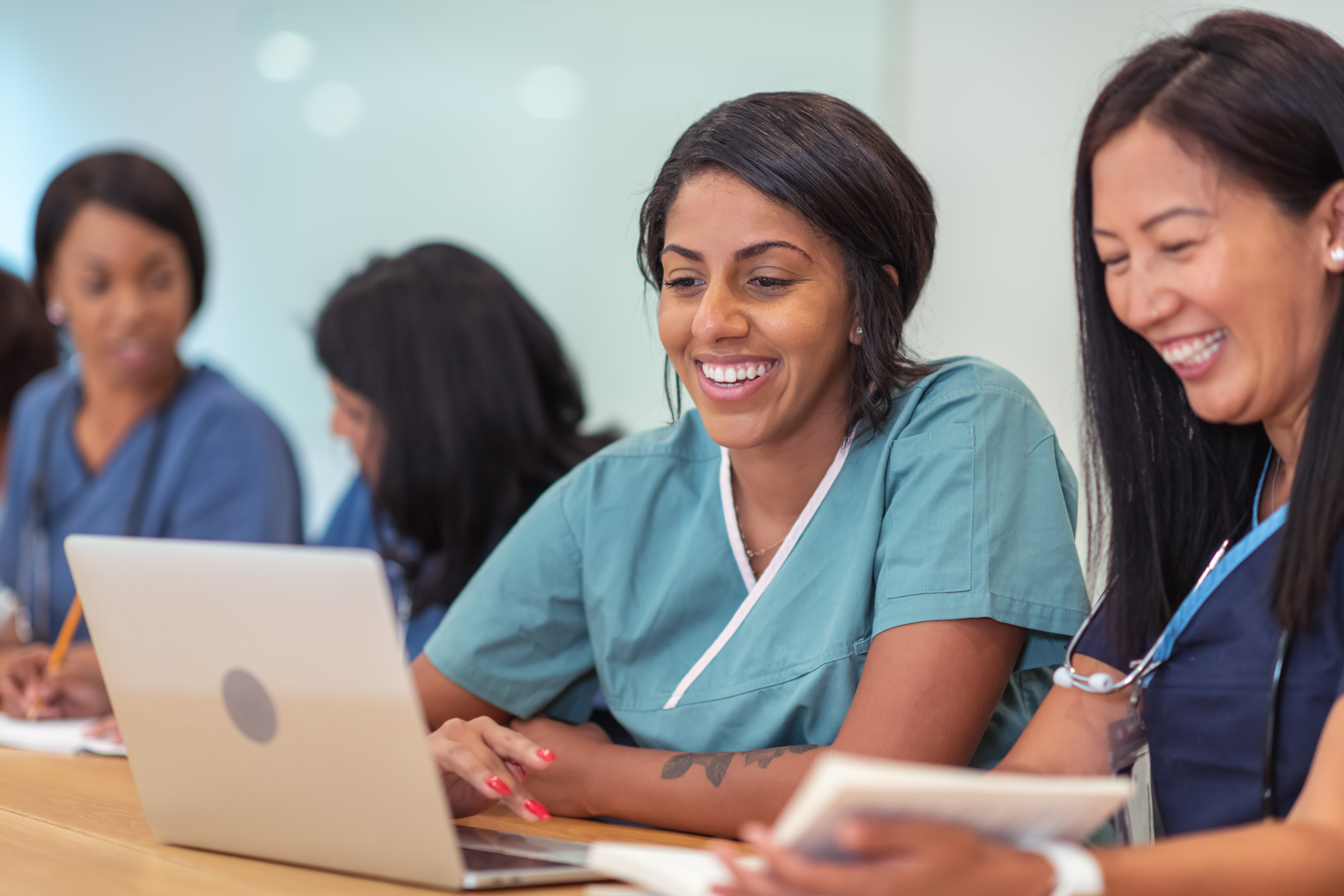 Female nurse smiling sitting at desk looking at laptop computer with other nursing students. Ultimate guide to Nursing Careers